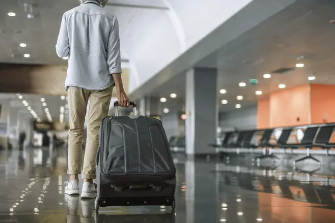 A person walking through a hall, pulling a large black suitcase